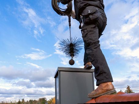 Technician atop a metal chimney chase with a sweeping brush